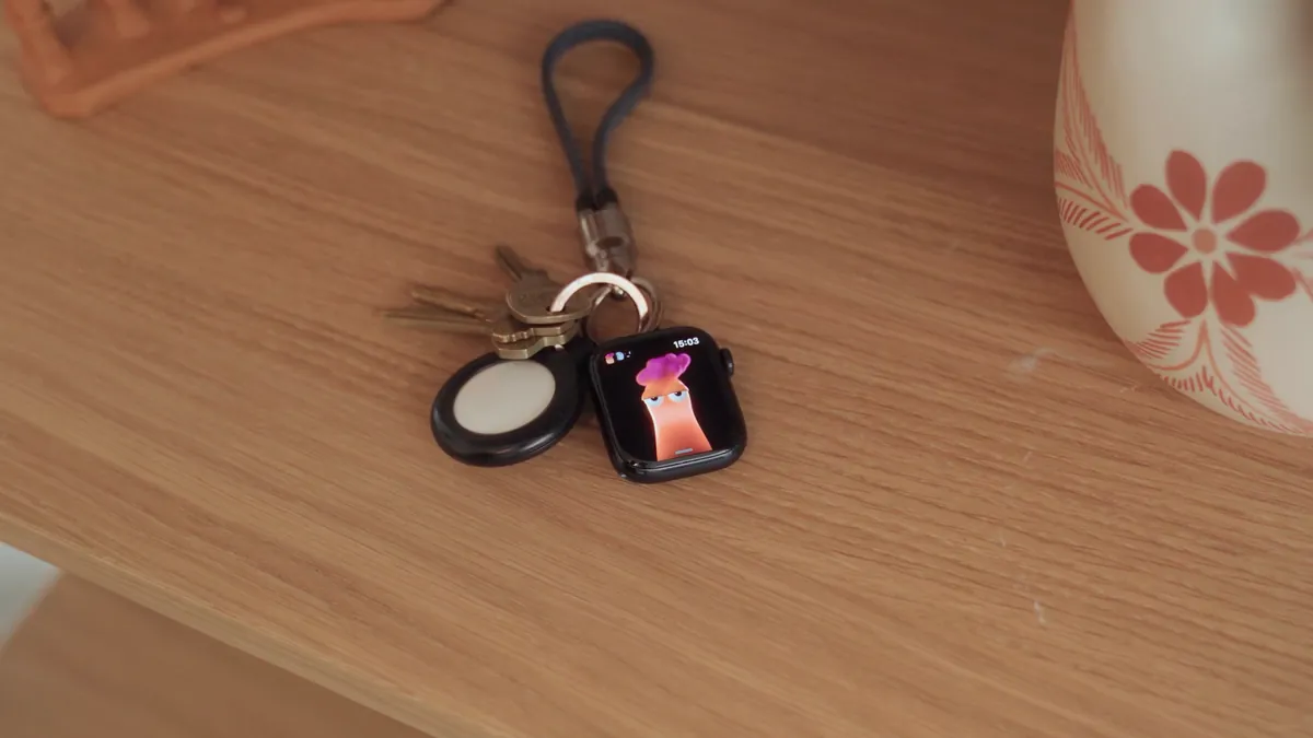 The watch on a keyring with keys and an AirTag, on a wooden shelf. Stretch is on the screen.
