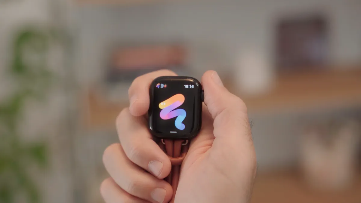 A hand holding the watch, without a band, on a leather lanyard. Noodle is on the screen.